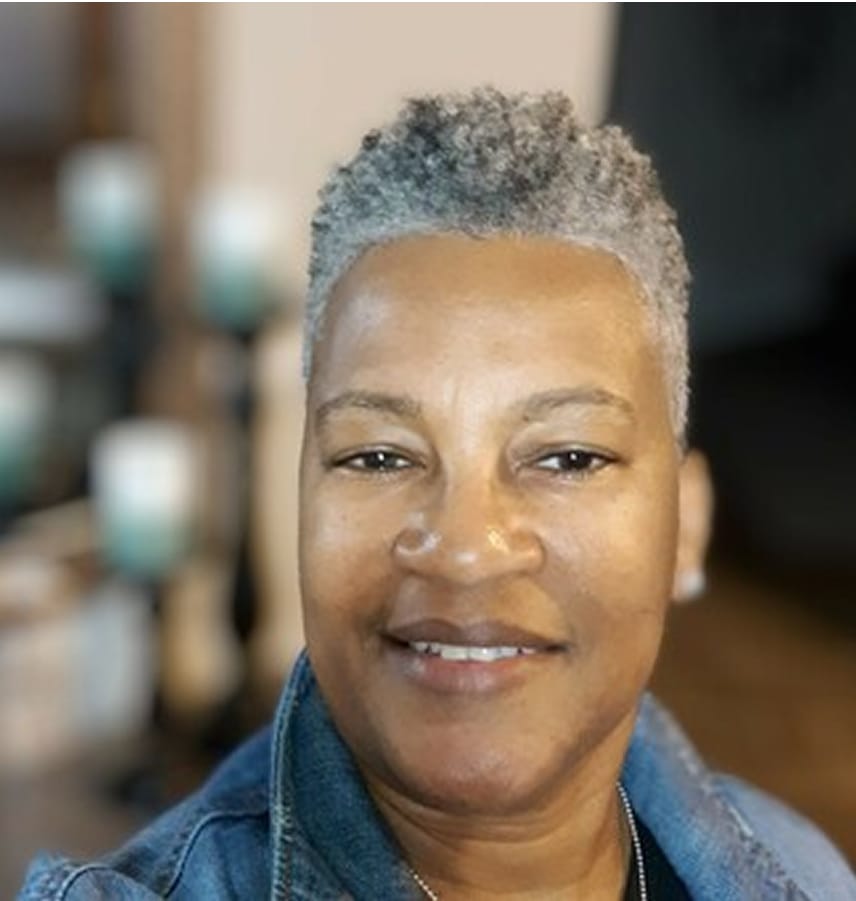 Smiling middle-aged woman with short curly gray hair wearing a denim jacket.