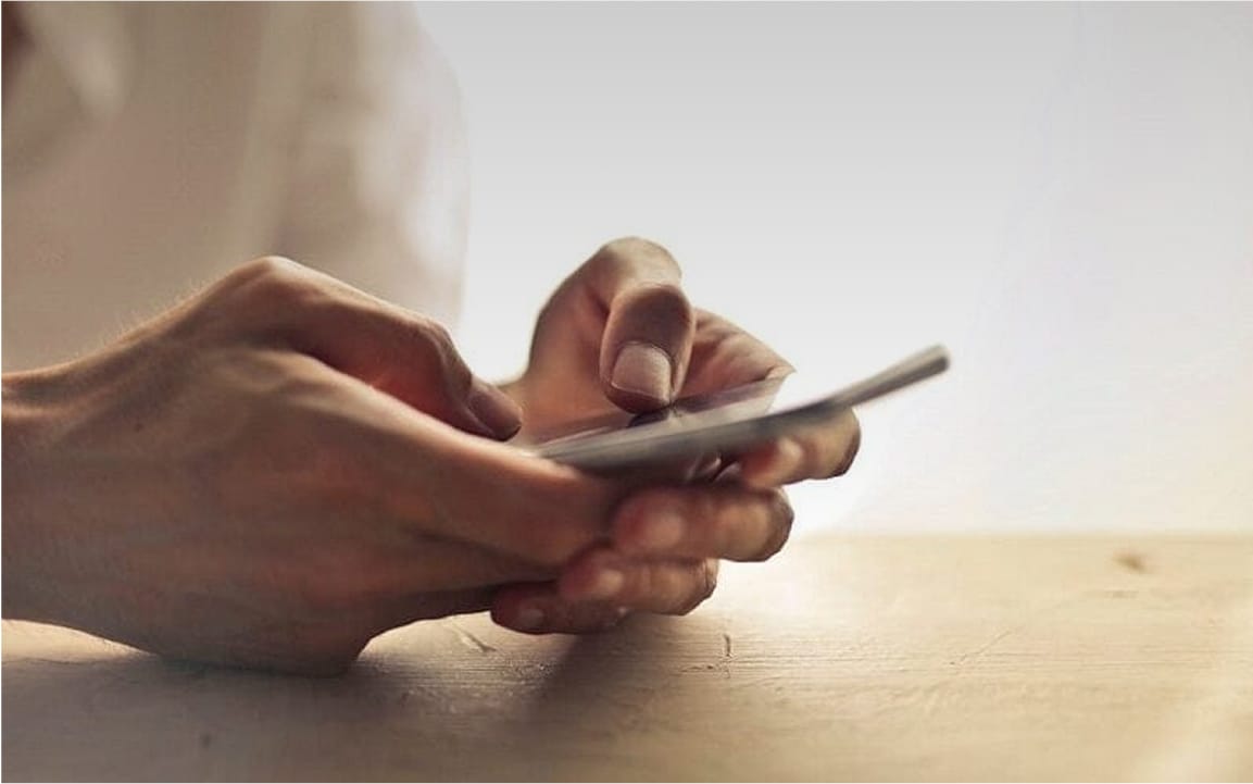 Close-up of hands holding and interacting with a smartphone over a wooden surface.