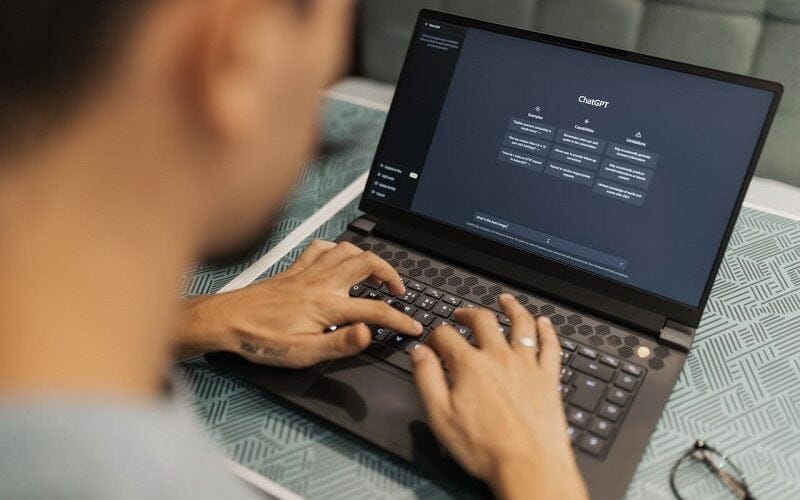 Person typing on a laptop displaying the ChatGPT interface on the screen.