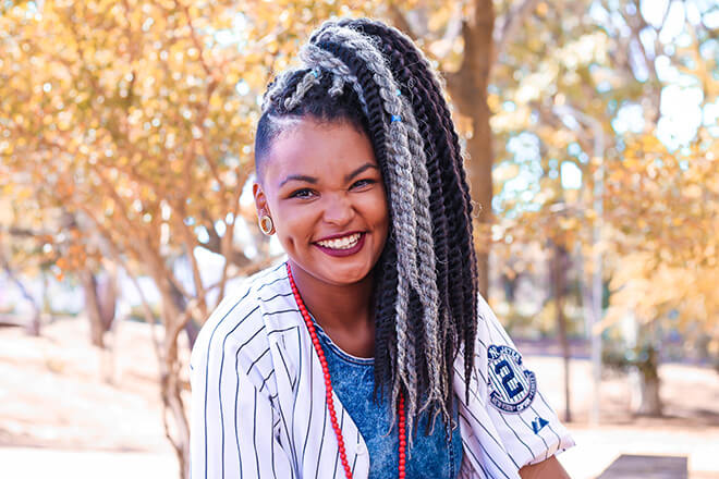 A woman with long hair and plug earrings smiles in a park