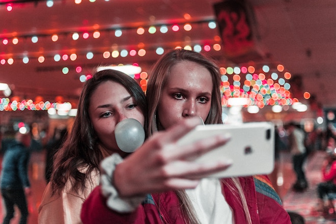 two women take a selfie while one blows a bubble