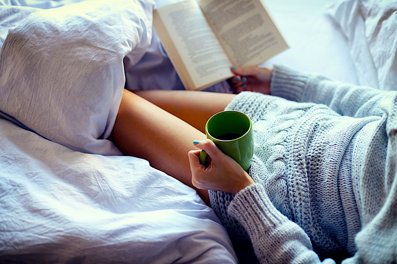 Person reading with tea under covers