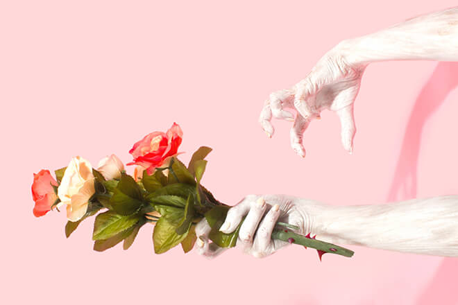 one hand holding flowers and another hand attacking that hand with a pink background