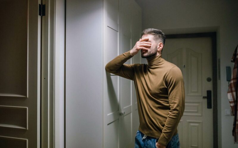 man standing against wall with hand on face