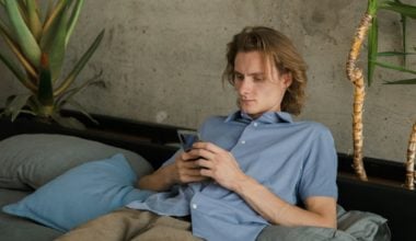 A guy looking at his phone while leaning back on a sofa