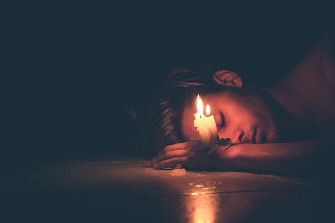 A man lays next to a candle in the dark