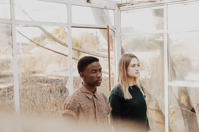 A couple stands in a house with broken windows