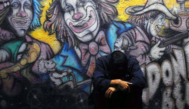 man looking down, clown graffiti behind him