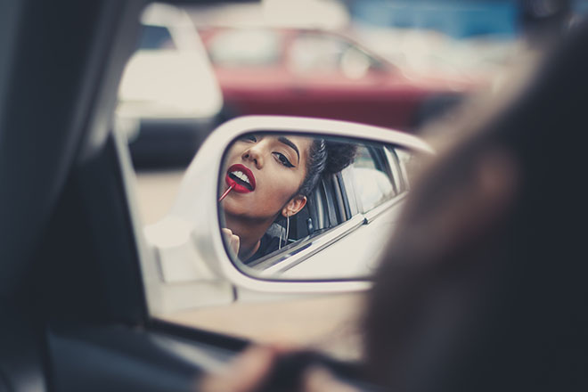 Woman putting make up on in a car mirror