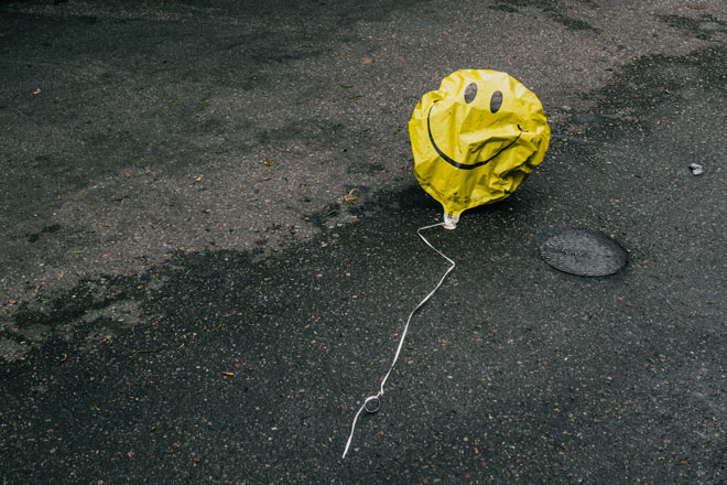 a deflated yellow smiley balloon on the street