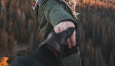 Woman holding a gloved man's hand on a mountaintop.