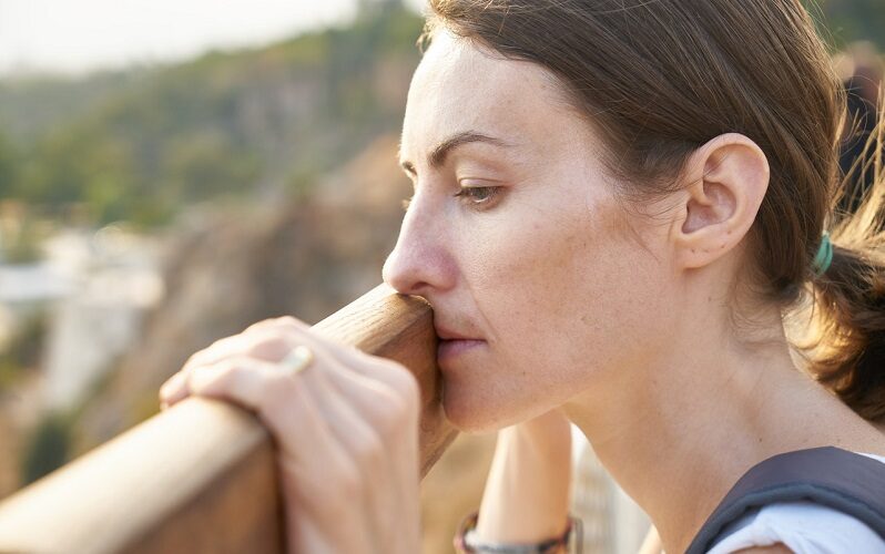 Sad woman standing on a wooden bridge leaning against the plank