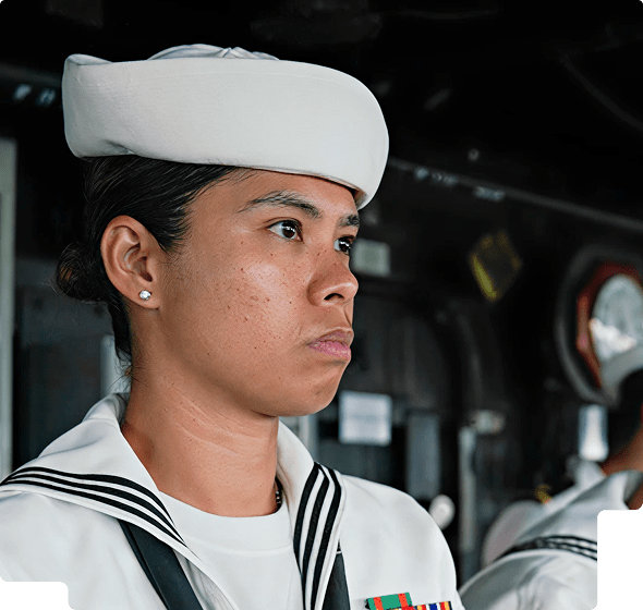 A focused female navy sailor wearing a white uniform and hat inside a ship.