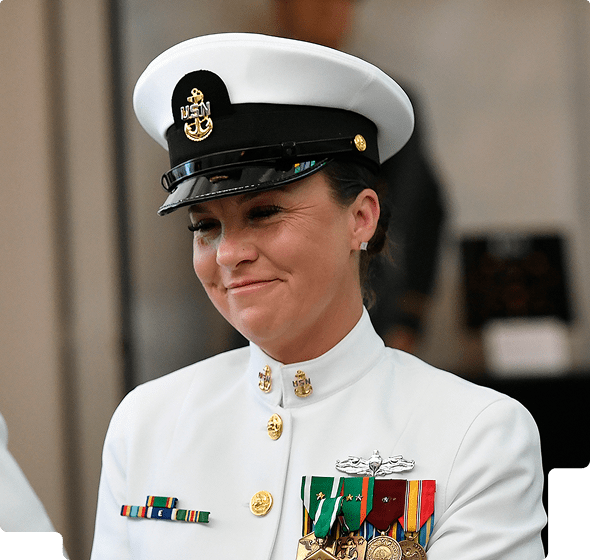 Female U.S. Navy officer in white dress uniform with medals smiling gently.